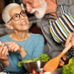 Gesund abnehmen: Älteres Pärchen beim Kochen in der Küche, im Vordergrund eine Salatschüssel.